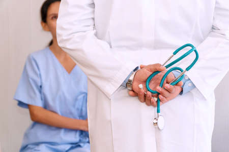 Behind back doctor holding stethoscope in his hands while patient woman sitting on the bed patient room at hospital. Professional doctor checking about patient sick healthcare at hospital room.の写真素材