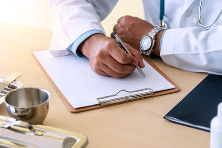 Doctor man holding pen ready to make notes only hands seen on table workplace. Doctor hand hold silver pen on patient with paper report on clipboard, physical check patient. Healthy lifestyle concept.の写真素材