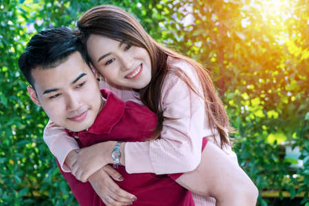 Cheerful young man giving piggyback ride to his joyful girlfriend while standing in the garden at home. Laugh couple having fun outdoor while woman holding arms around boyfriend. Relationship concept.の写真素材