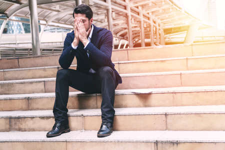 Businessman bankruptcy and debt with hands cover face while sitting on the stairs.Unemployed businessmen frustrated and desperate to find work. Concept business people failure and unemployment problemの写真素材