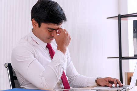 Handsome young businessman sitting with laptop on table working place at office while massaging his...
