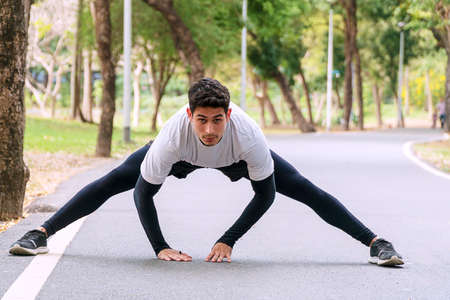 Athlete young man stretching shoulder before workout in the park. Trainer male warming up...
