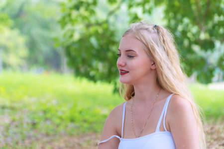 Cheerful young woman blonde long hair looking away while sitting alone in the park. Beauty cute...