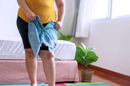 Oversize fat young woman trying to wear short jeans. Overweight female in tight pants jeans or clothing worried about weight gain. Plus size model girl with cellulitis.Obesity and weight loss concept.の写真素材