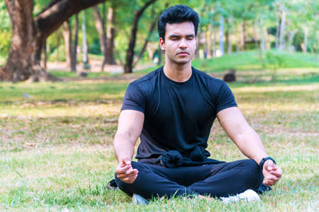 Handsome young indian guy practicing yoga in the park Serene yoga man practitioner workout and sitting in lotus pose or asana with closed eyes. Yoga and meditation healthy conceptの写真素材