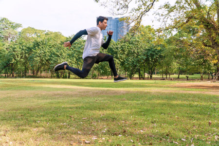 Handsome young man athlete runner with energy exercise training and jumping outdoors with big green...