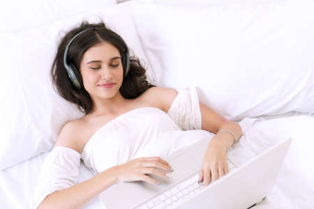 Attractive young woman with earphones listening to music form laptop while lying eyes closed on...