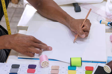 Hand of woman holding pen in her hand while drawing sketches on paper In fashion design studio....