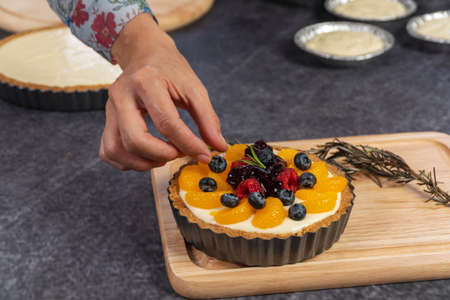 Hand of young woman decorating blackberry pie using fresh fruits on table. Homemade bakery concept.の写真素材