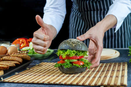Hand of chef man thumb up with set vegetable hamburger on table over black background. Homemade bread burger concept.の写真素材