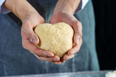 Close up hand of chef man wearing grey apron while holding homemade raw dough in heart shape.の写真素材
