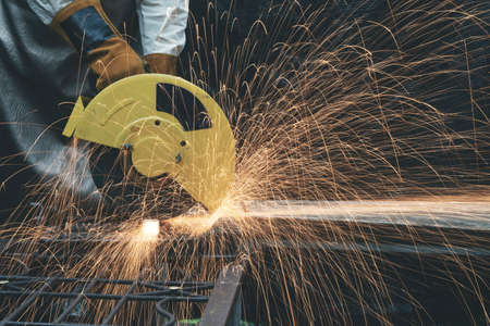 Hands of man with glove using electric steel cutter machine while working at workshop. Male cutting steel with sparks flying. Hard work in factory or garage industry in construction site concept.の写真素材