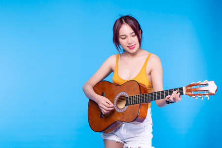 Happiness young woman play music with acoustic guitar on blue background. Portrait cheerful female...