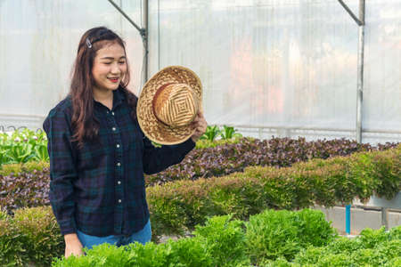 Young woman standing on the greenhouse with hat in her hand hot weather day while feeling tired...