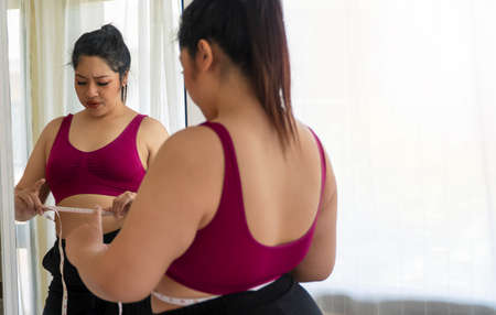 Obesity unhealthy concept. Reflection of overweight woman wear sport bar with measure tape on body...