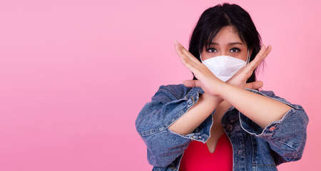 Protective safety outbreak virus and heath care concept. Obesity fat woman wear protection face mask using arm hand making symbol stop no flu over isolated pink background.の写真素材