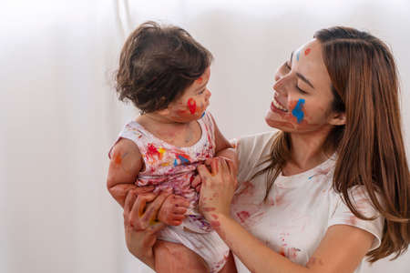 Joyful motherhood hugging own infant daughter with face painting watercolor while playful together...