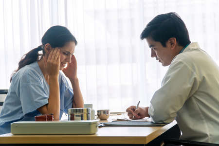 Health care concept. Professional young man doctor with pen in his hand explaining problems headache patient woman while sitting together talking in the office room at hospital.の写真素材