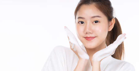 Adorable young woman washing her face with foam soap in hand while standing over isolated white background. Skin care and cosmetics conceptの写真素材
