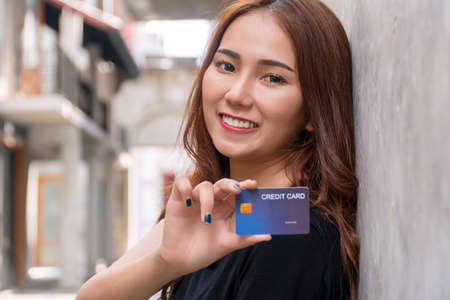 Payment banking concept. Business woman get satisfy and happy with freedom of finance money. Smiling young woman showing credit card mockup looking to camera on gray with city background. Select focusの写真素材
