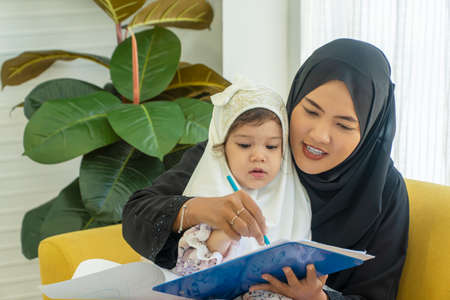 Family lifestyle activity education concept. Daughter mix race girl wear headdress hijab learning...