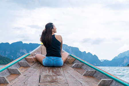 Adventure lifestyle vacationer relax concept. Traveler young woman holding own hair while sitting on long tail boat floating lagoon with mountains and sky while vacation tourist at surat thani.の写真素材