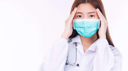 Failure outbreak covid-19 health care concept. Unhappy tired doctor or nurse woman wear uniform coat and medical face mask holding hand on own head while standing over isolated white background.の写真素材