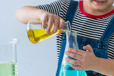 Student genius trust education science concept. Hands of little boy scientist holding lab bottle with experiment water chemical in his hand on table with microscope while study in the white room.の写真素材