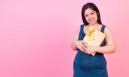 Celebration happy new year,  Christmas,anniversary, birthday concept. Smiling fat woman holding gold gift box in her hand while standing with copy space over isolated pink background.の写真素材