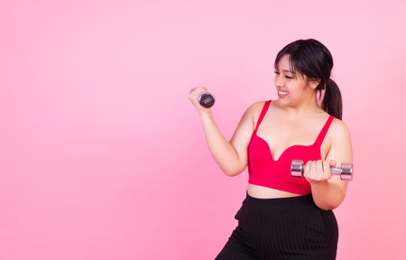 Exercise bodybuilding diet healthy care concept. Chubby obesity plus- size smile woman holding dumbbells workout for weight loss while standing over isolated pink background.の写真素材