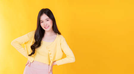 Confident charming Asian young woman wear hipster style standing over isolated yellow background. Cheerful student or businesswoman smart success while looking at camera.の写真素材
