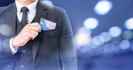 Payment expenses finance concept.Hand of businessman wear suit put or take out credit card in pocket on bokeh background. Handsome young man takes out blank business card from his front pocket suit.の写真素材