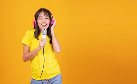 Enjoy singer Asian young woman wear casual with pink headphones listen music holding microphone sing...