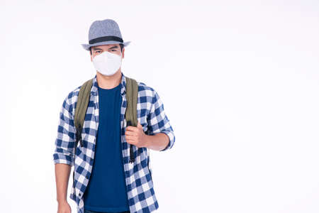 Traveler adventure handsome man wear casual shirt, hat and protective mask safety with backpack standing over isolated white background. New normal lifestyle travel vacation concept.の写真素材