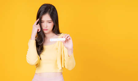 Unhappy young woman stress head showing positive antigen test coronavirus while standing with copy space over isolated yellow background. New normal lifestyle concept.の写真素材