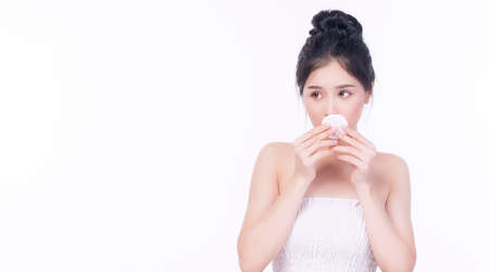 Portrait of asian young woman holding white cotton pad on own mouth for removing make-up on isolated on white background. Healthy skin and cosmetics concept.の写真素材