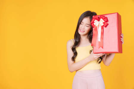 Surprise greeting anniversary birthday or celebration christmas and new year. Cheerful excited young woman holding red gift box with ribbon in own hand while standing over isolated blue background.の写真素材