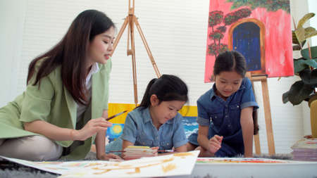 Asian two siblings learning study watercolor paint together at home. Teacher or parent teach student or daughter drawing paint color imagination on paper homework.Activity creativity education conceptの写真素材