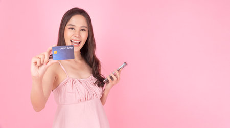 Cheerful excited asian woman holding smart phone and mockup credit card or debit for internet...