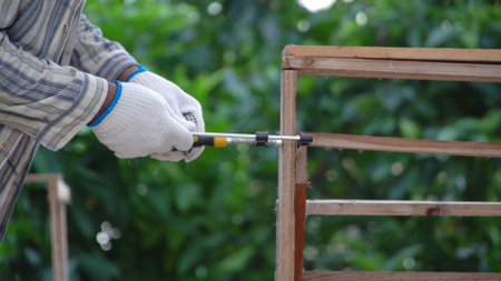 Hands of craftsman woodworker handmade diy wood table furniture tools at workplace on green nature background. Hands of carpenter wear gloves builder diy furniture production at home. Hobbies woodworkの写真素材
