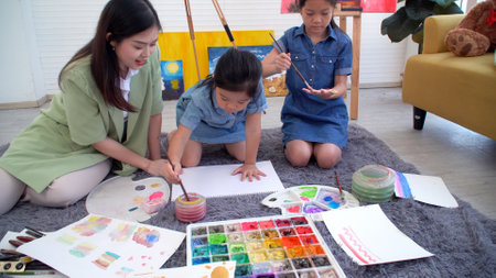 Asian two siblings learning study watercolor paint hand together at home. Teacher or parent teach student or daughter use hand paint color imagination on paper homework.Activity creativity educationの写真素材