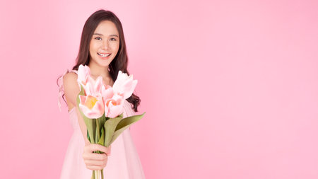 Satisfied excited asian woman holding tulips pointing up wonder to copy space smiling with toothy standing over isolated pink background. Cheerful young girl use tulips flower pointing present productの写真素材