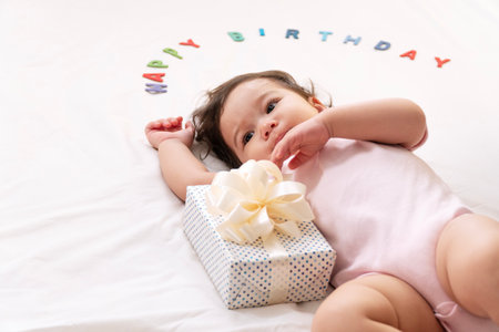 Innocence asian toddler lying down with white gift ribbon box character happy birthday looking to parent on bed at home.Happiness Little daughter received gift box birthday one year growth family careの写真素材