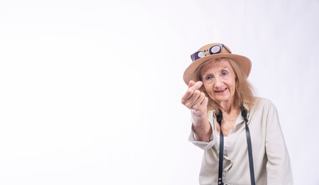 Cheerful traveler elderly woman using finger sign mini heart standing over isolated white...