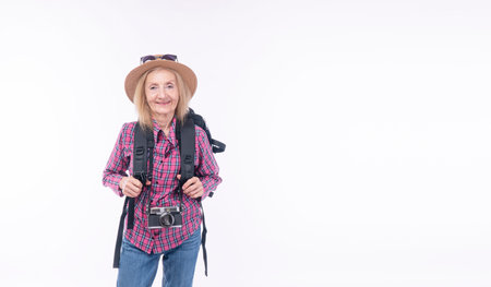 Healthy active cool elderly woman casual jeans with backpack hat standing over isolated white background. Cheerful retired female sunglasses on hat hold camera carefree vacation adventure holiday.の写真素材
