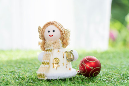 Angel figurine with decoration red ball symbol Christmas on fresh green grass nature background. Cute angel doll decoration merry xmas celebration festive on meadow ornament garden background.の写真素材