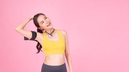 Cheerful sporty woman stretching body after sport over isolated pink background. Healthy active young girl sportswear with wireless earphones armband refreshing after sport stretch body looking empty.の写真素材