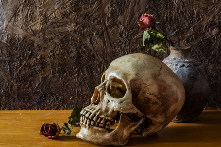 Still life with human skull with red rose in the old vase  on wooden floorの写真素材