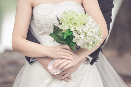 Married bride and groom embracing each other with a bouquet of flowers as a symbol of love and happiness.の写真素材