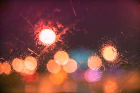 Abstract bokeh blur background by rain drops on glass window at night in the city